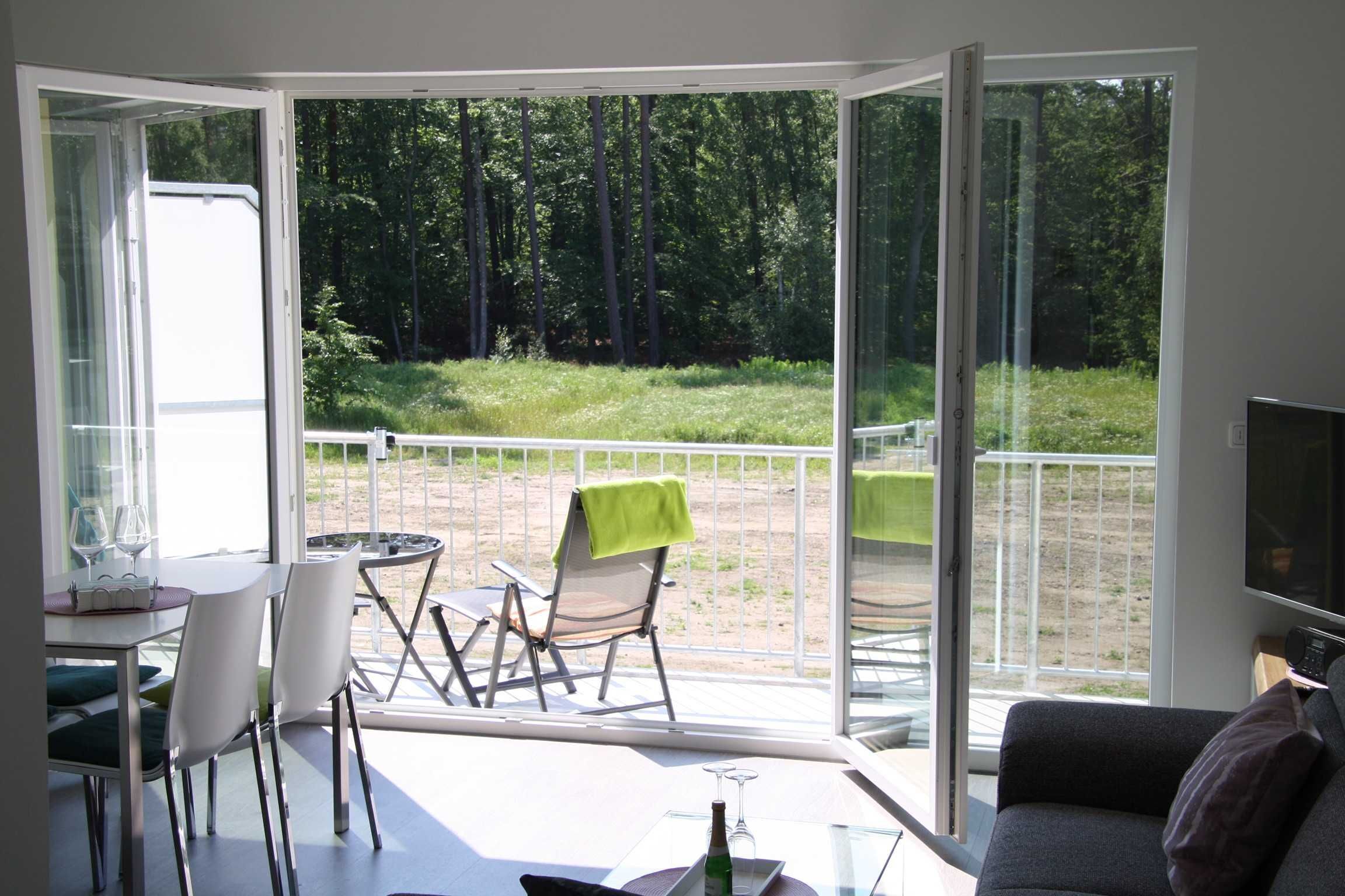 Un salón moderno con un ventanal de vidrio que da a un patio exterior. Hay un comedor con mesa y sillas, y un sofá en el salón.