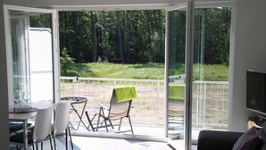 A modern living room with a glass door leading to an outdoor patio. There is a dining area with a table and chairs, and a sofa in the living room. - *öddeker, Lidia und Dieter GM 69137 - Holiday apartment in the coastal forest - Baltic Sea SNR: (Gelbensande)