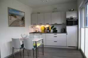 A modern kitchen with white cabinets, a dining table with chairs, and a painting of a beach scene on the wall.