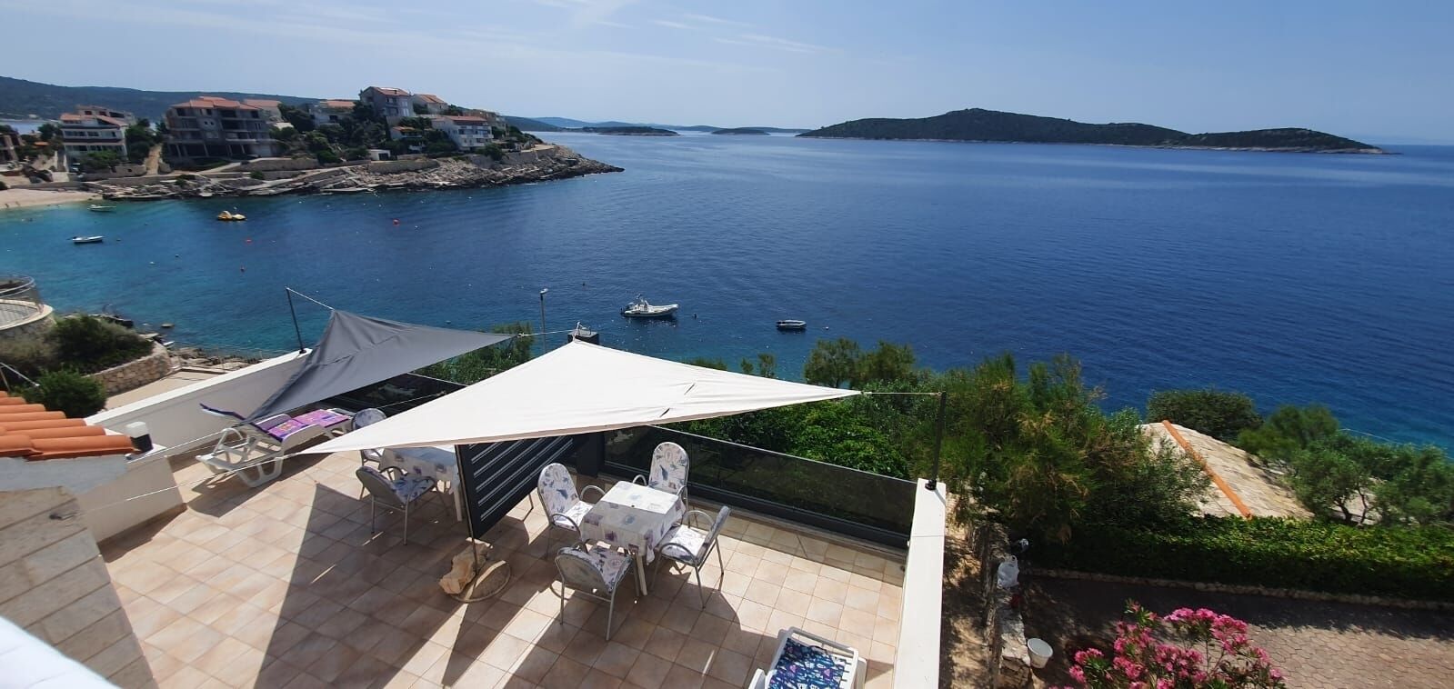 Um terraço com mesa e cadeiras, com vista para uma área costeira com barcos e edifícios.