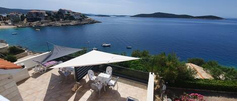 A terrace with a table and chairs, overlooking a coastal area with boats and buildings.