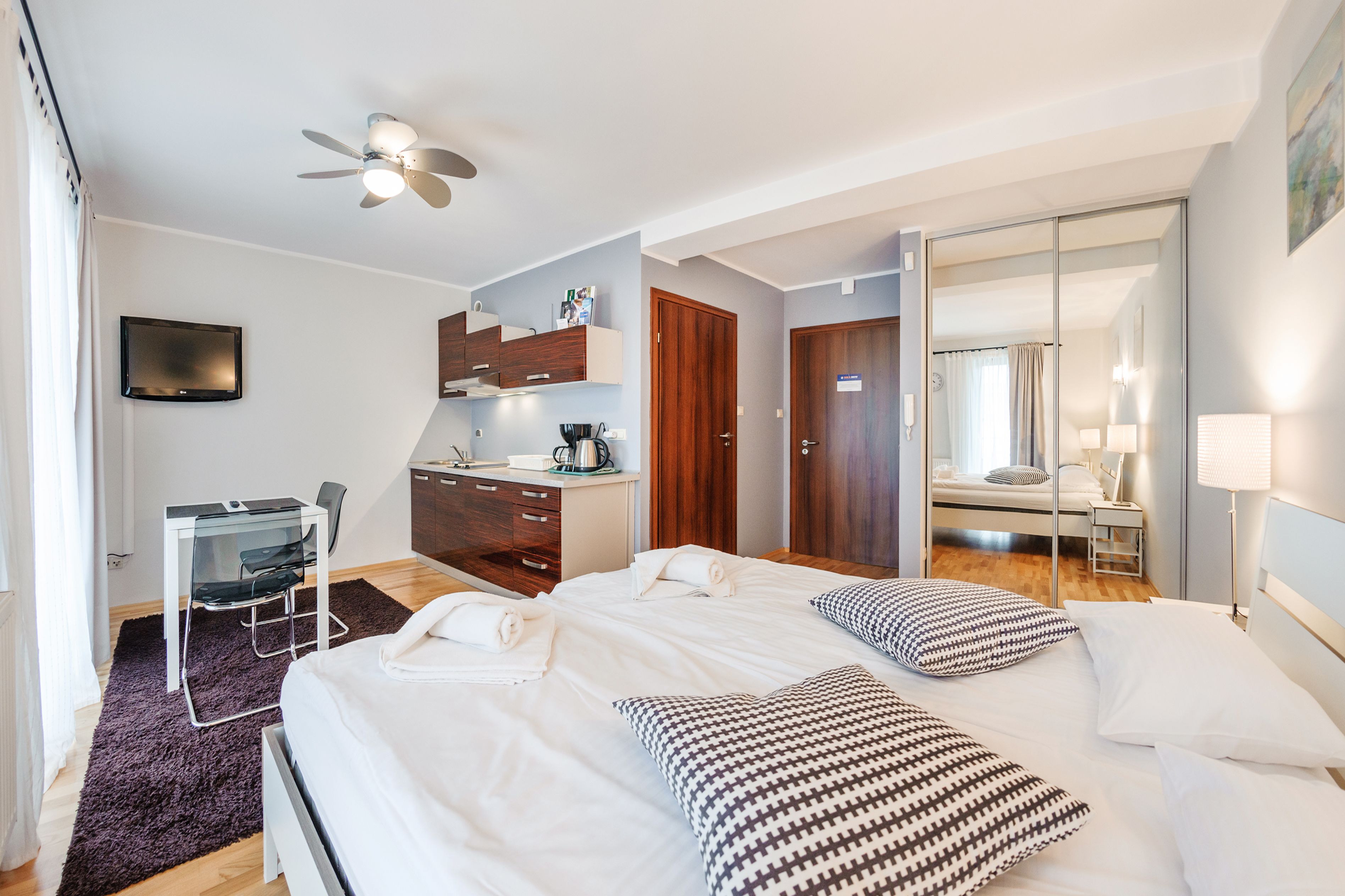A modern hotel room with a large bed, a desk with a chair, a wardrobe, and a bathroom visible through an open door.