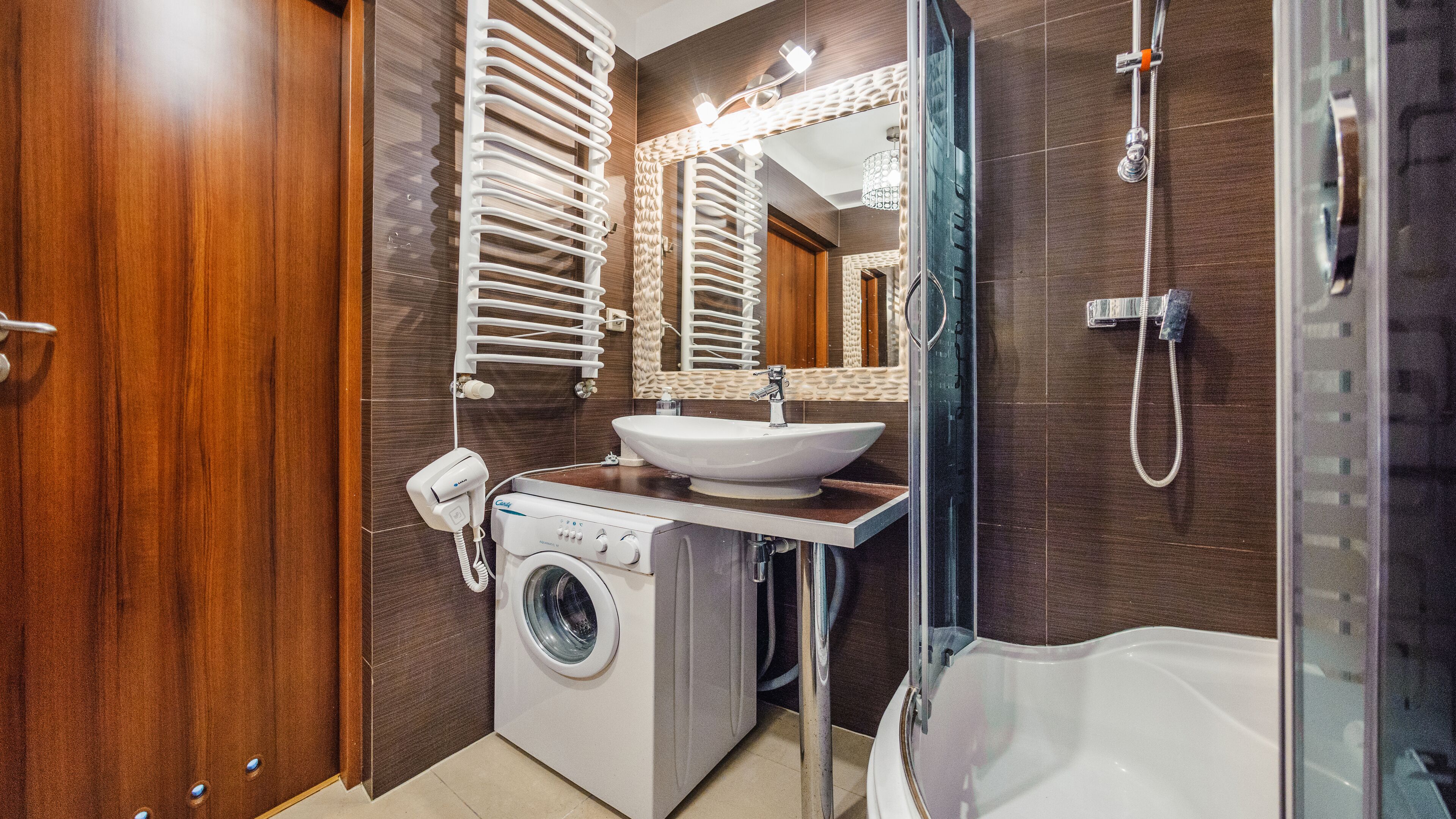 A modern bathroom with a wooden vanity, a sink, a washing machine, and a shower.