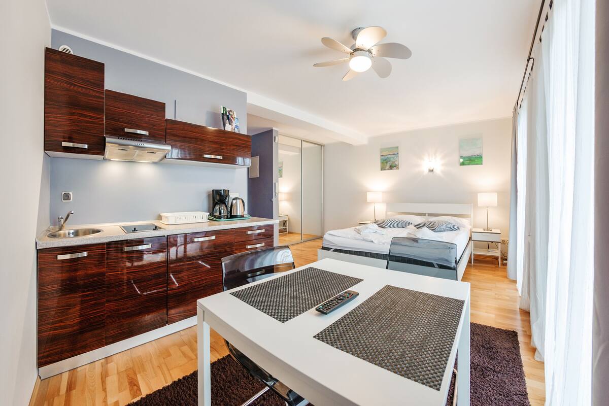 A modern hotel room with a kitchenette, a bed with a view, and a dining area.