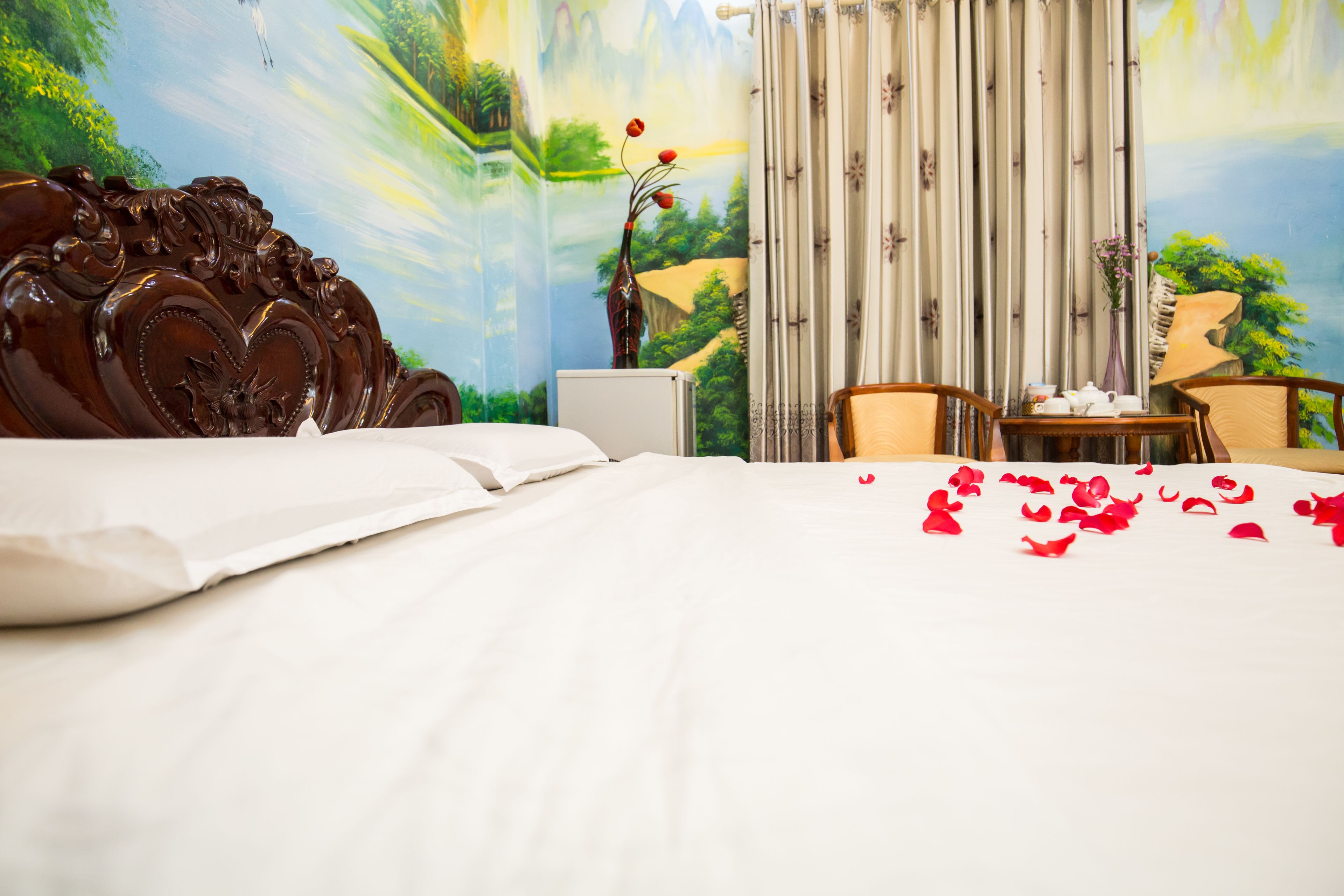 A hotel room with a large bed, a laptop on a bedside table, and a view of a scenic mural.