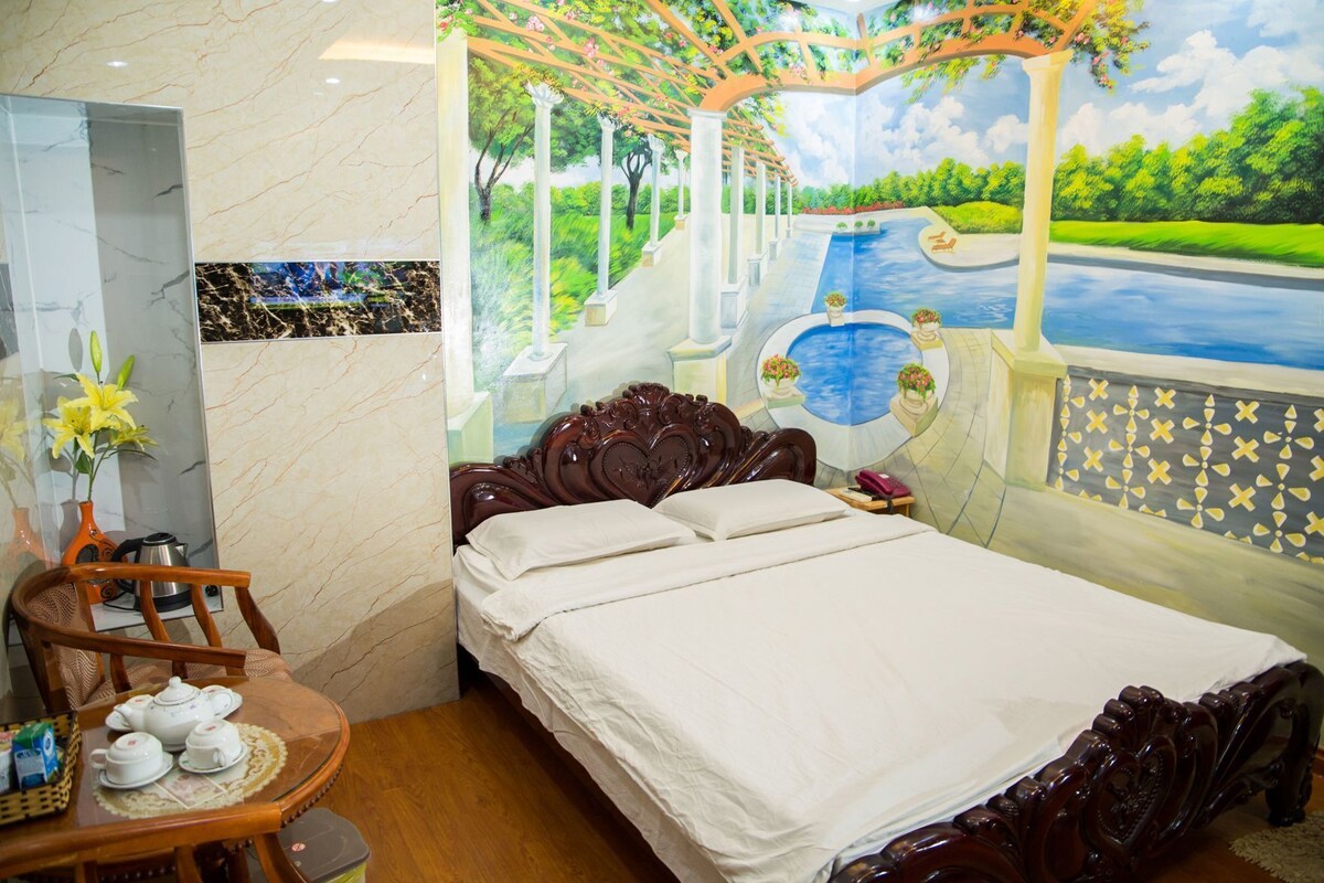 Un dormitorio con una cama, una silla, una mesa con un jarrón y teteras, y un mural de un jardín y una piscina.