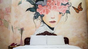 Un dormitorio con cama, ropa de cama blanca, cabecera de madera, mesita de noche con teléfono y un jarrón de flores.