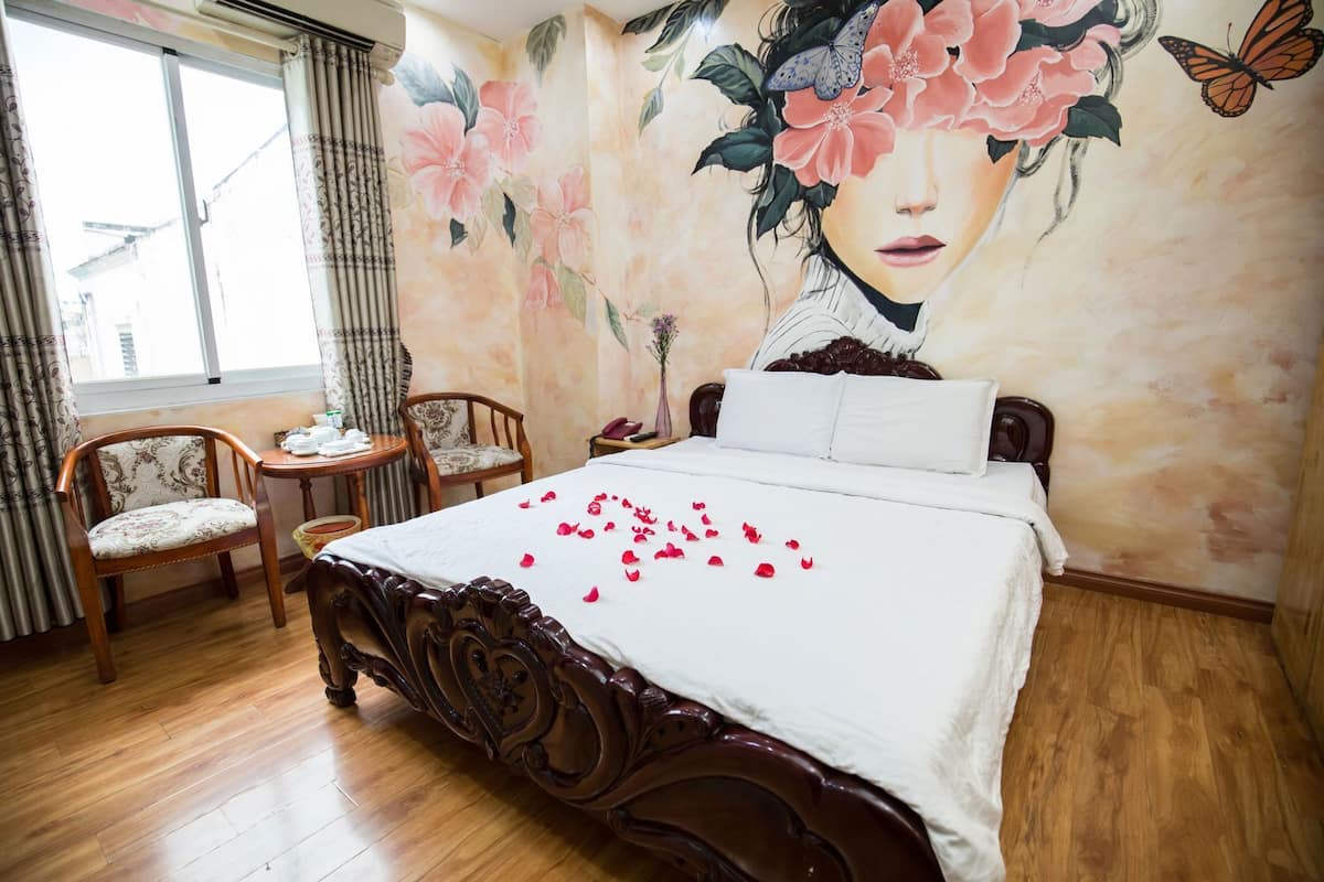 Une chambre avec un grand lit, deux chaises, une petite table et une fresque florale sur le mur.