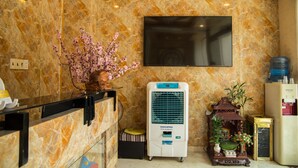 Un área de recepción con pared de mármol, un televisor de pantalla plana, un aire acondicionado Daichiro y un pequeño santuario con dispensador de agua.