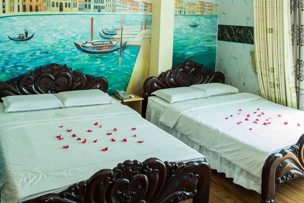 Une chambre d’hôtel avec deux lits, une fresque représentant un paysage de canal et un luminaire au plafond.