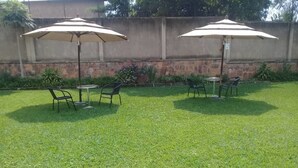 A patio area with two tables and chairs, each under a large umbrella. - Kami Executive Apartments (Kigali)