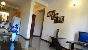 A living room with a glass coffee table, a television, and a small black table. - Kami Executive Apartments (Kigali)