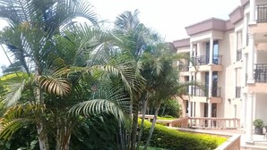 A residential building with balconies, a well-maintained garden with palm trees, and a paved walkway. - Kami Executive Apartments (Kigali)