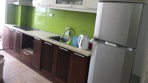 A kitchen with a stainless steel refrigerator, a sink with a green backsplash, and wooden cabinets. - Nhimhouse   Hanoi... (Thanh Xuân)
