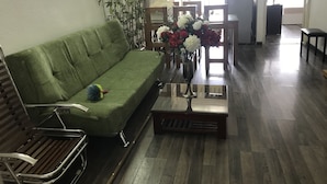A living room with a green sofa, a wooden coffee table with a vase of flowers, and a wooden chair. - Nhimhouse   Hanoi... (Thanh Xuân)