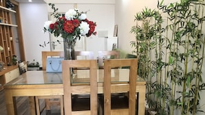 A dining area with a glass-top table, wooden chairs, and a vase of flowers. - Nhimhouse   Hanoi... (Thanh Xuân)