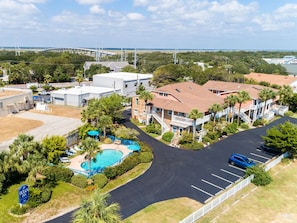 Um hotel com piscina, estacionamento e vista para uma ponte ao fundo.