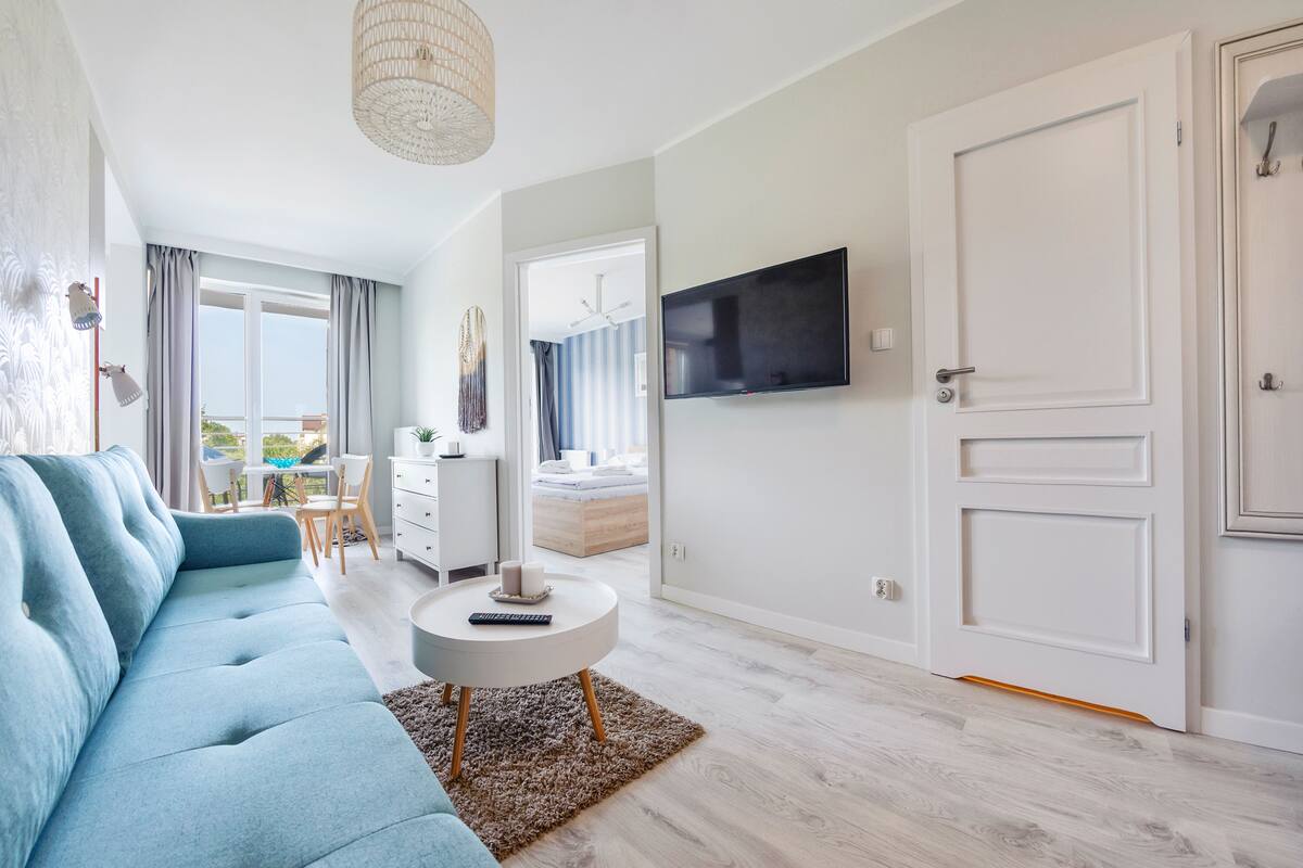 A modern living room with a blue sofa, a round coffee table, and a flat-screen TV mounted on the wall.