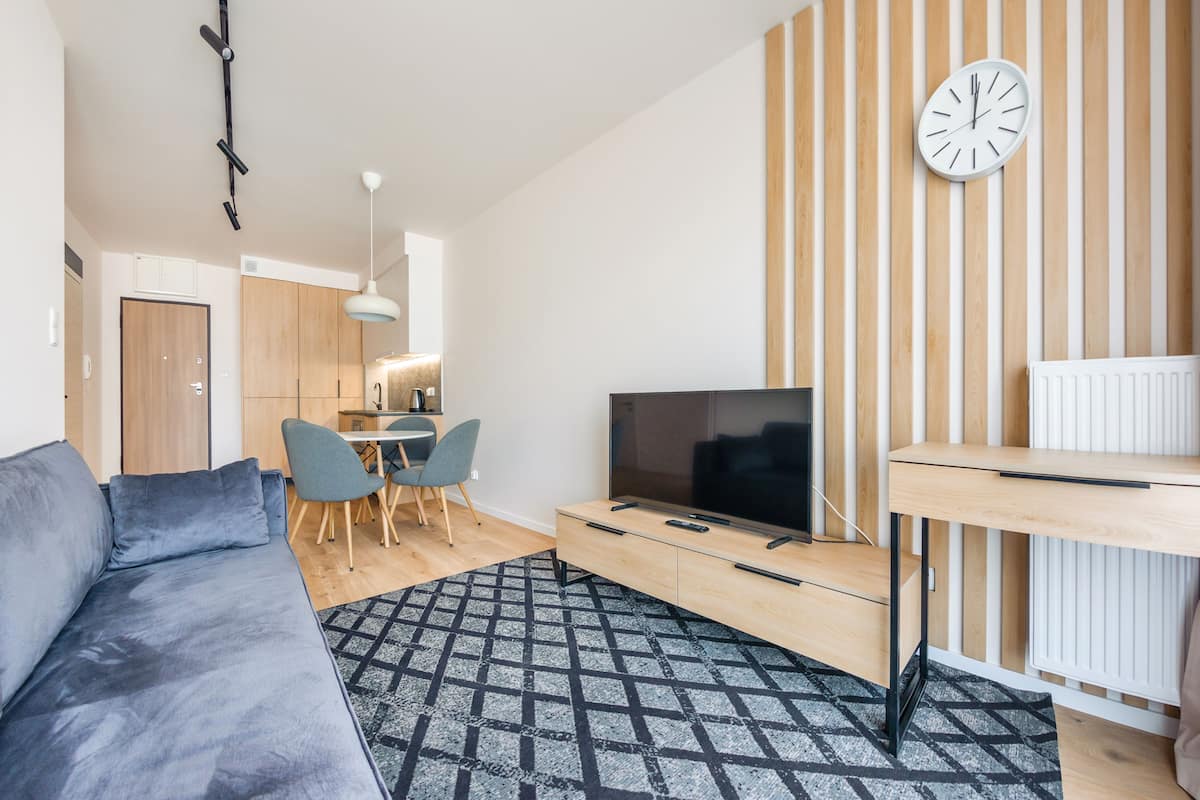A modern living room with a sofa, TV, wooden panel wall, and a clock.