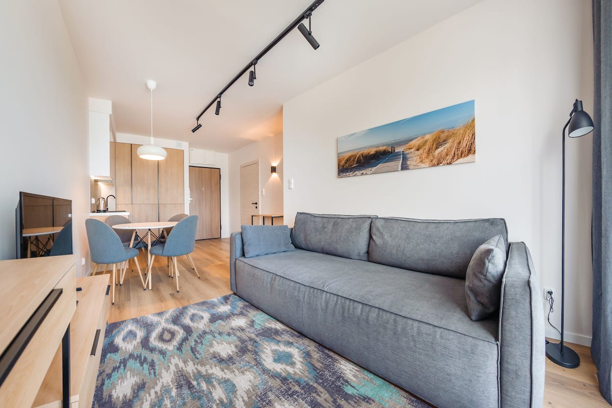 A modern living room with a grey sofa, blue chairs, a wooden dining table, and a patterned rug.