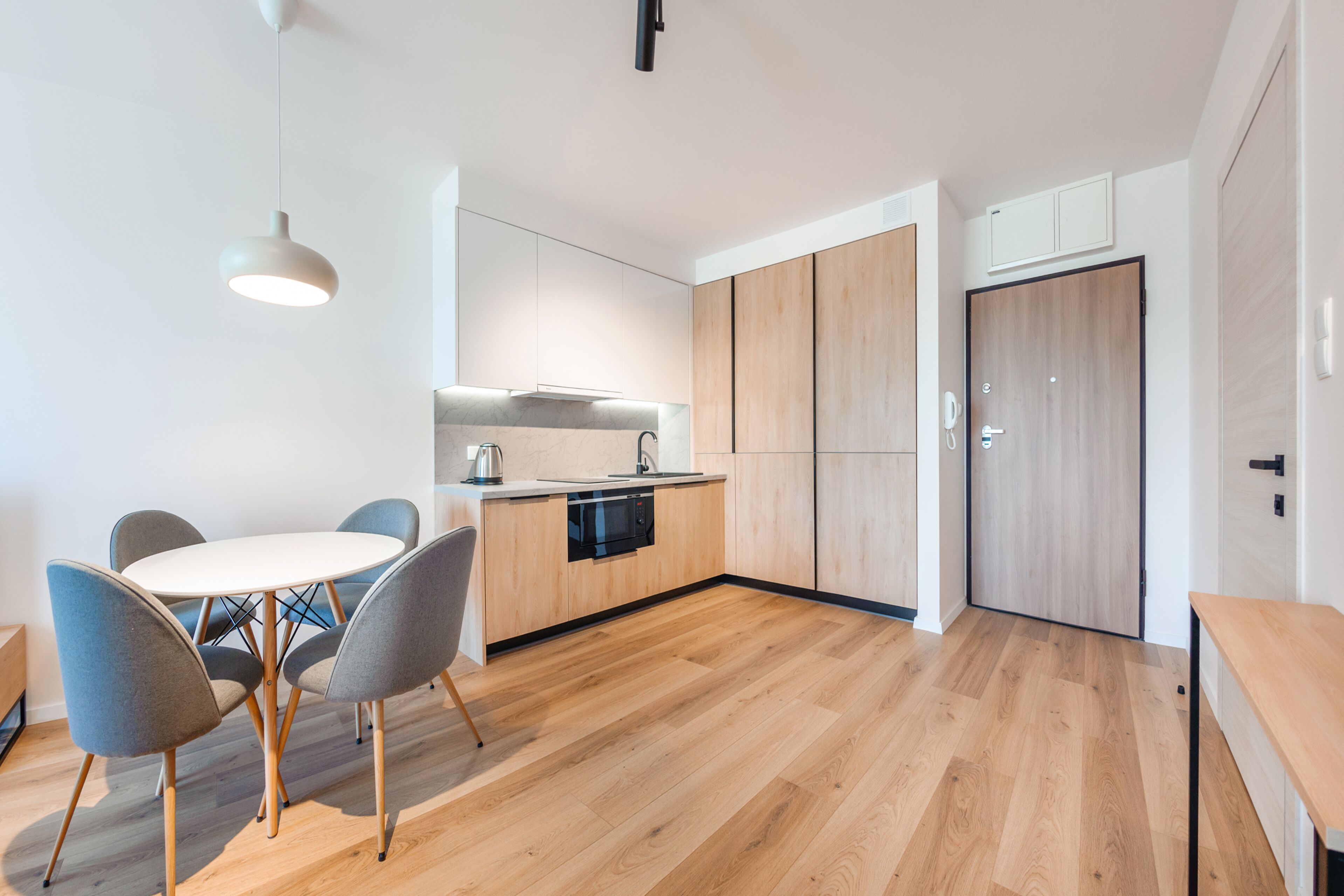 A modern kitchen with wooden cabinets, a built-in oven, and a dining area with a round table and chairs.