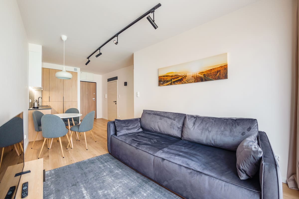A modern living room with a grey sofa, a dining table with chairs, and a kitchen area in the background.