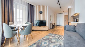Una sala de estar moderna con televisión, sofá, comedor y cocina al fondo.