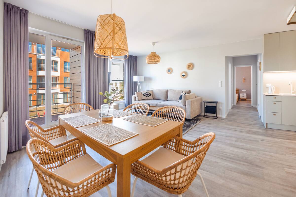 A modern living room with a dining area, a sofa set, and a kitchen visible through an open door.