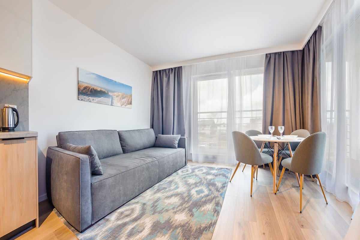 A modern living room with a grey sofa, a coffee table, and a dining area with chairs and a table.