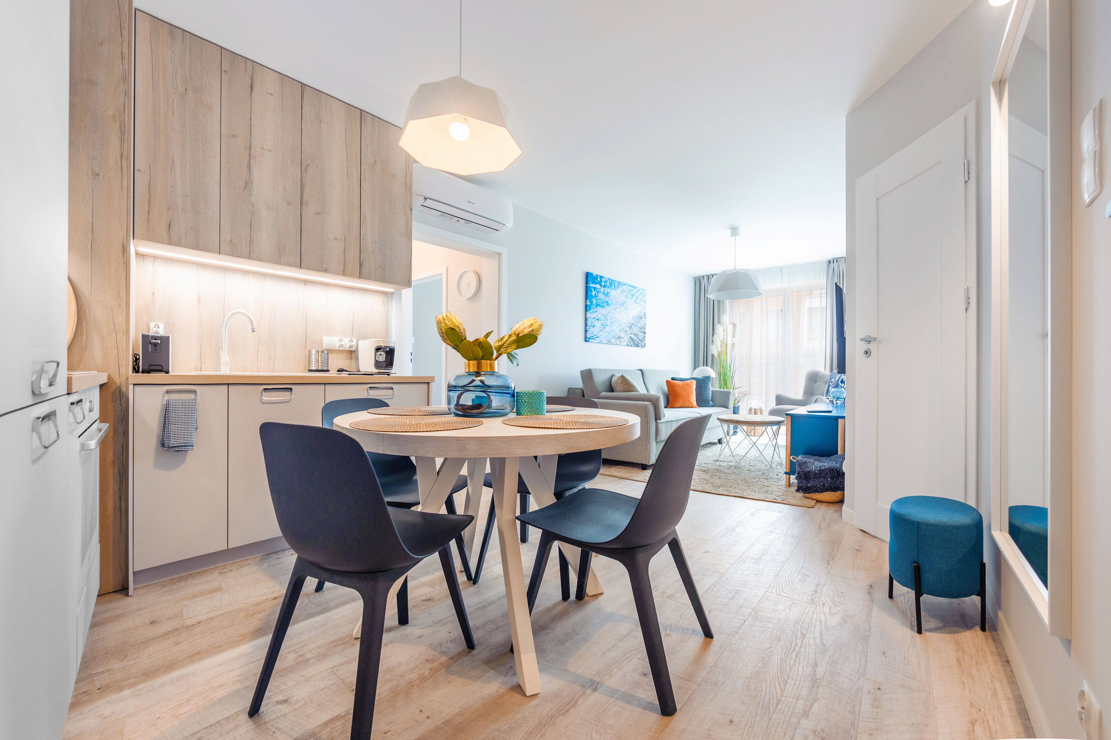 A modern kitchen with a dining area, wooden cabinets, and a round table with chairs.