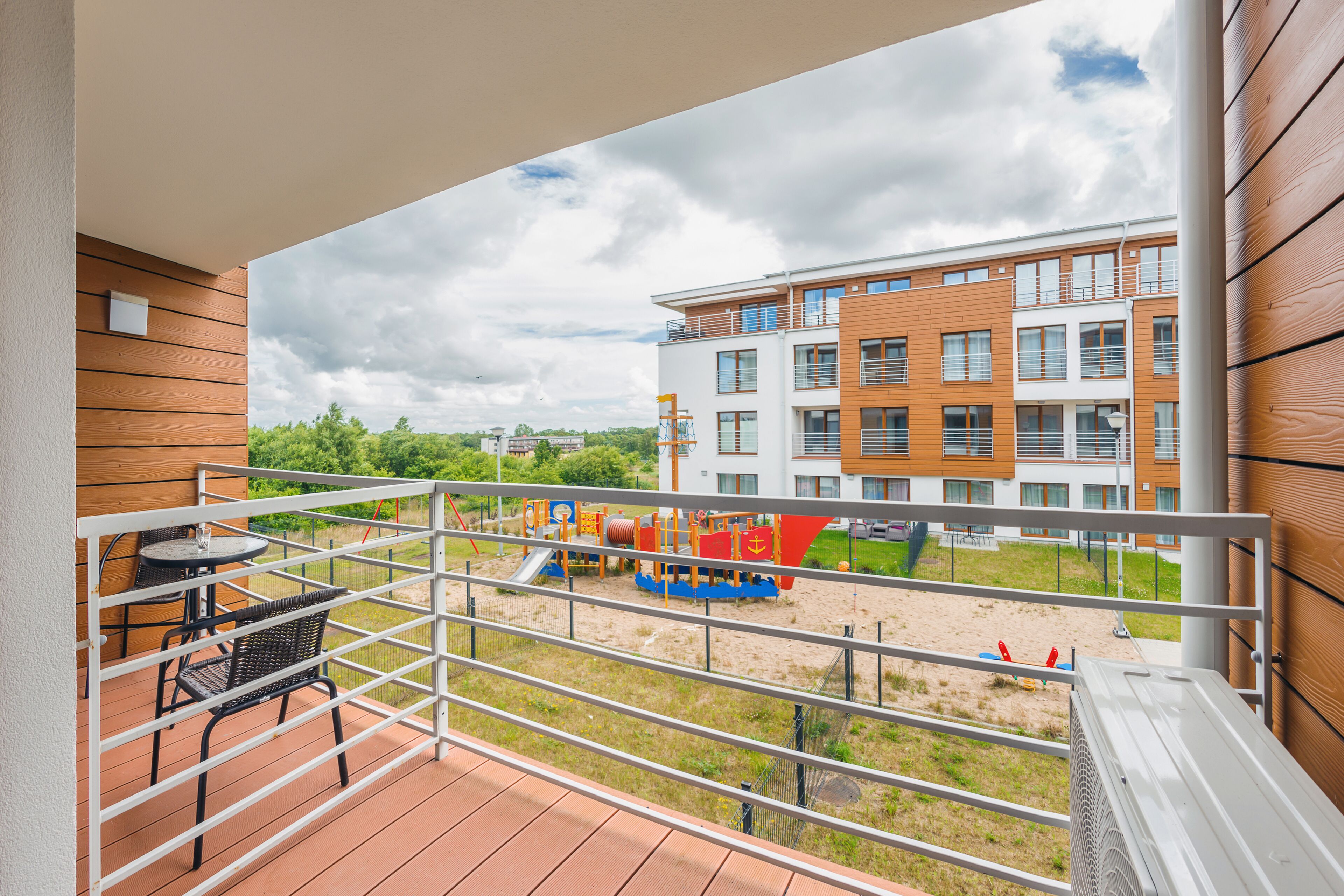 A balcony with a view of a playground and a multi-story building.
