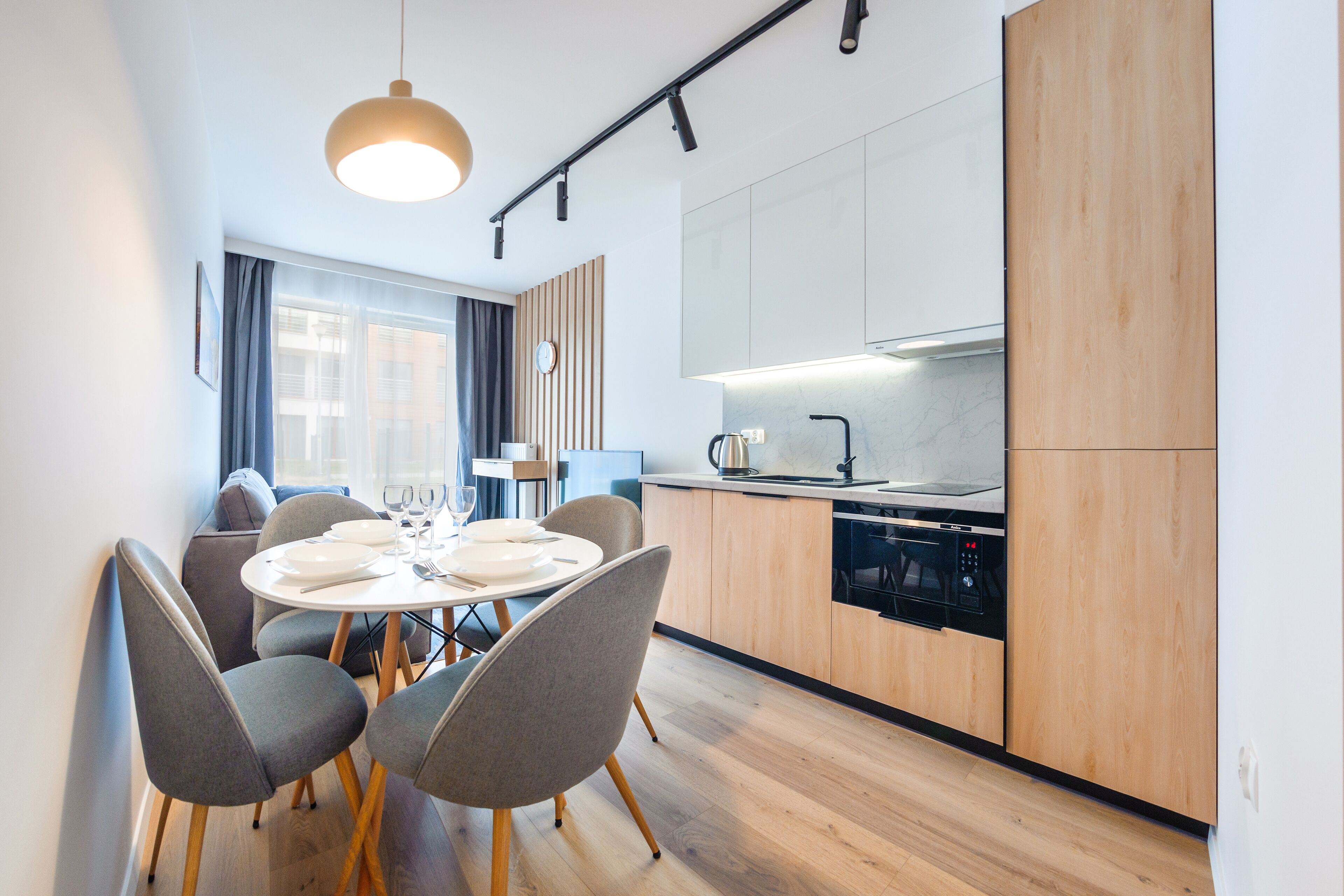 Une cuisine moderne avec des meubles en bois, un four encastré et un coin repas comprenant des chaises grises et une table ronde.