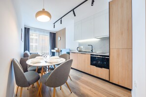 A modern kitchen with wooden cabinets, a built-in oven, and a dining area with grey chairs and a round table.