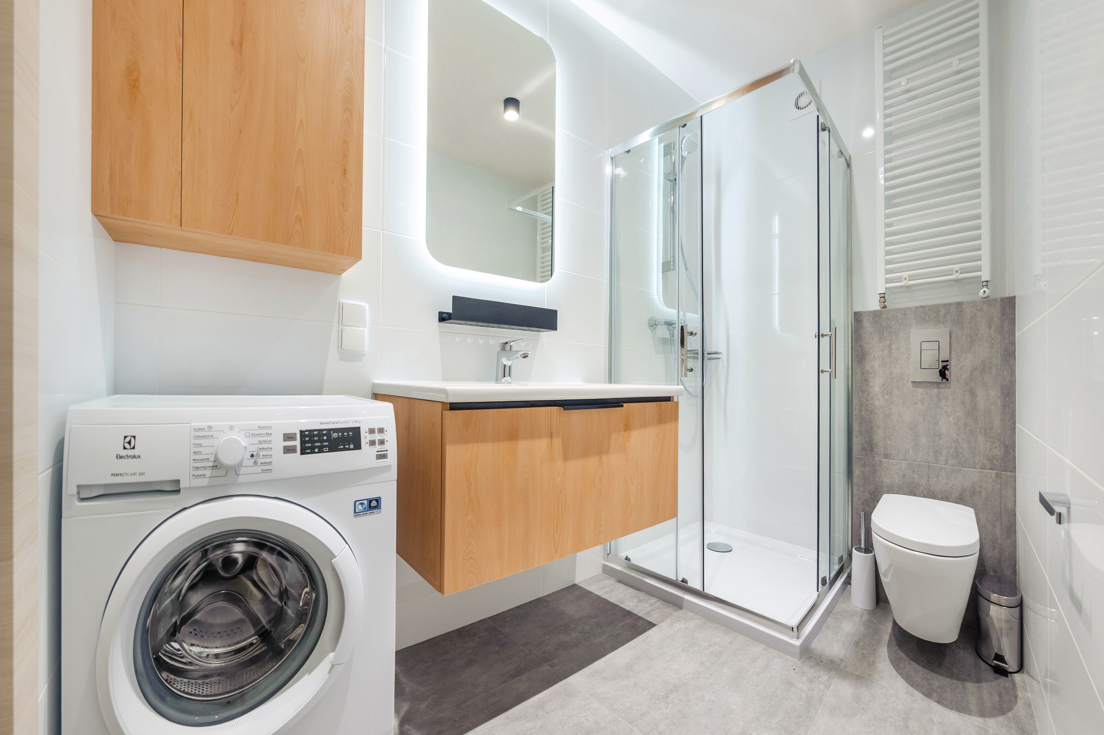 A modern bathroom with a washing machine, a glass shower enclosure, and a toilet.