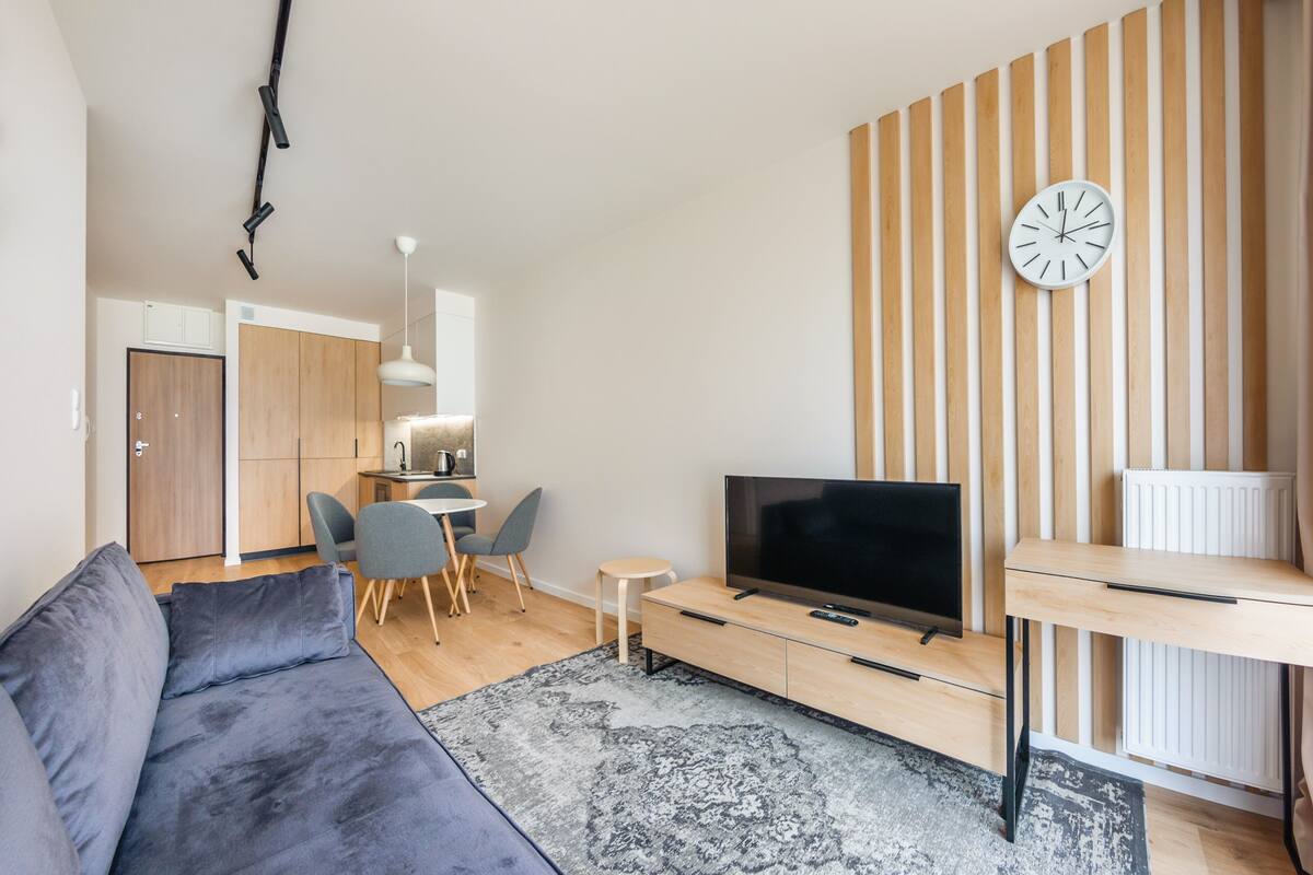 A modern living room with a sofa, TV, and a dining area with chairs and a table.