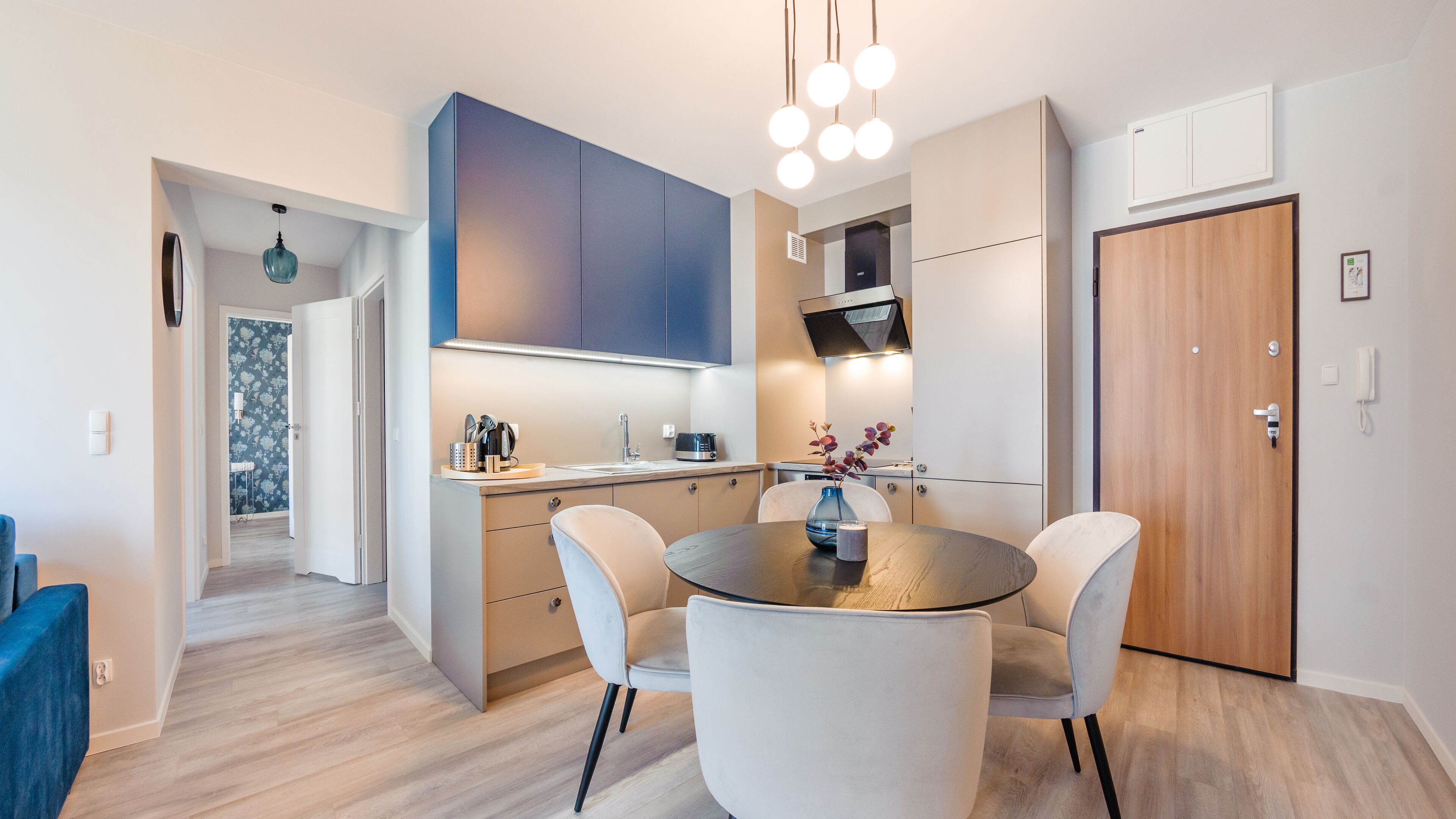 A modern kitchen with a round dining table, white chairs, and a blue vase.