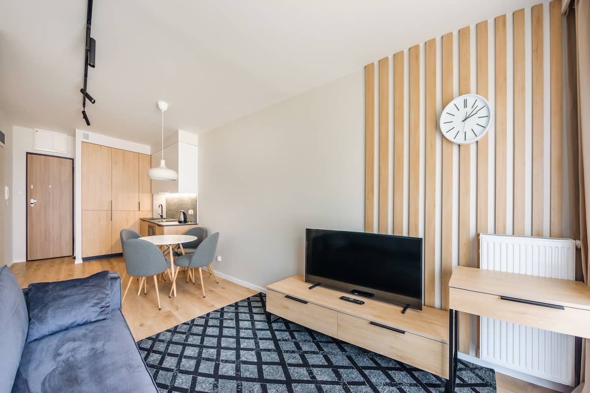 A modern living room with a flat-screen TV, a dining area with chairs, a sofa, and a patterned rug.