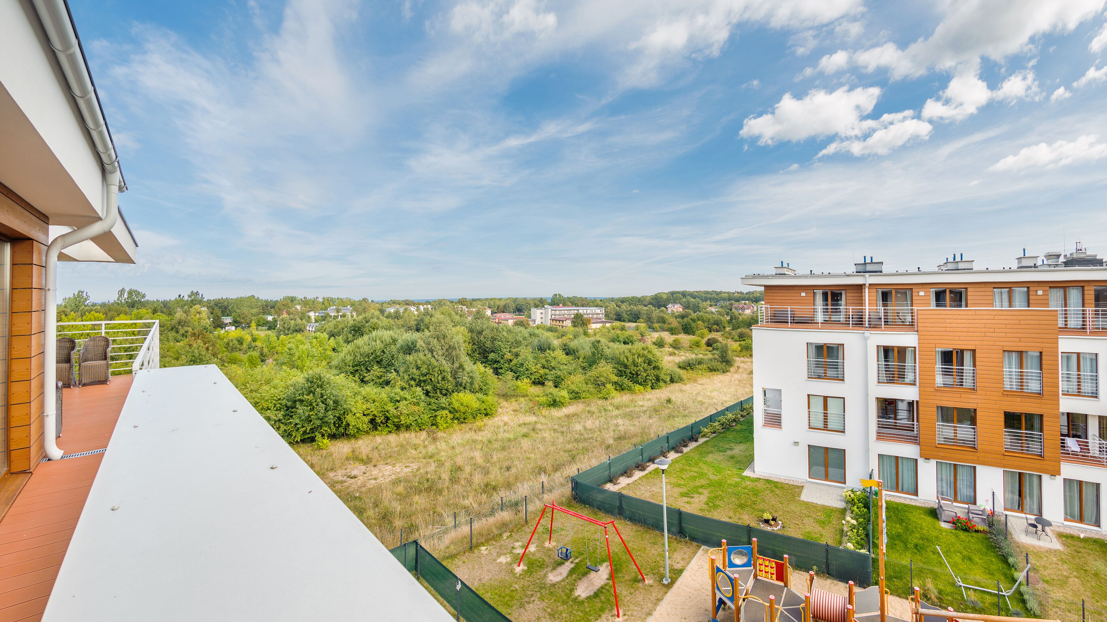 Een woongebouw met een balkon, een schommel en uitzicht op een groen landschap en andere gebouwen.
