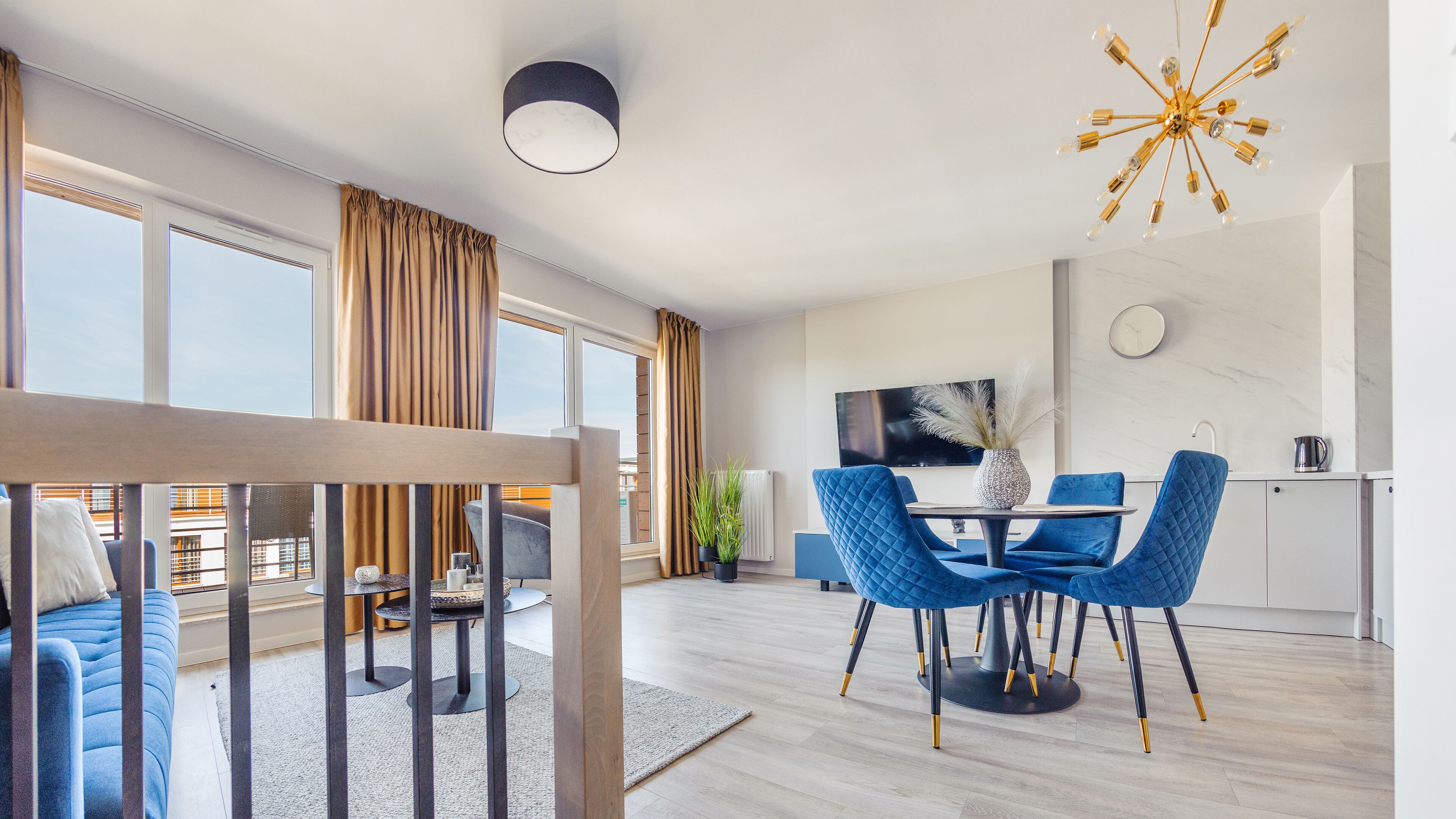 Una sala de estar moderna con comedor, ventanas amplias, un televisor de pantalla plana y una zona de cocina con hervidor.