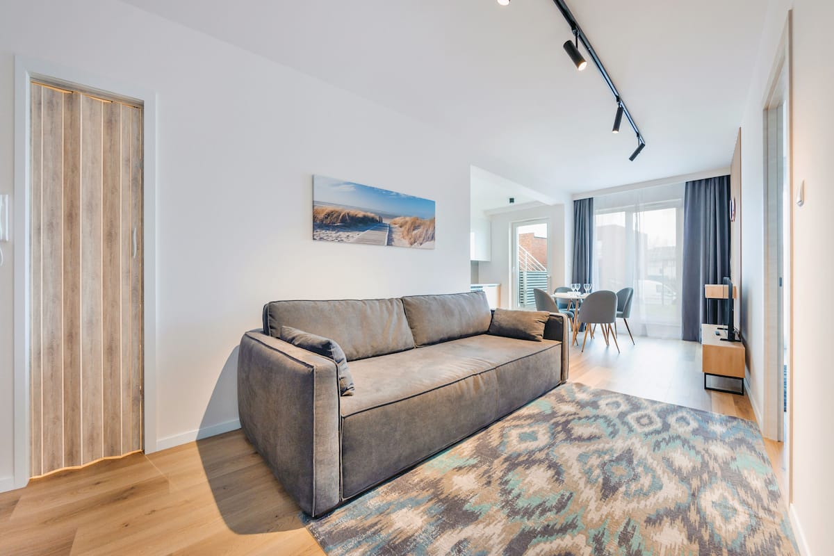 A modern living room with a sofa, a patterned rug, a wooden door, and a dining area with chairs and a table.
