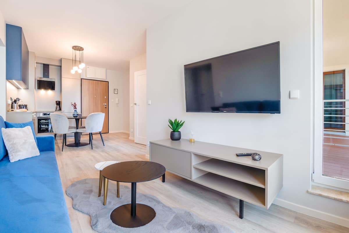 A modern living room with a blue sofa, a round coffee table, and a TV mounted on the wall.