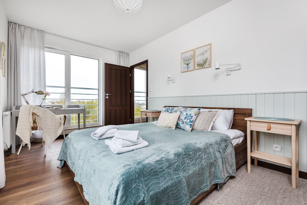 A bedroom with a bed, bedside table, and a view of the outdoors.