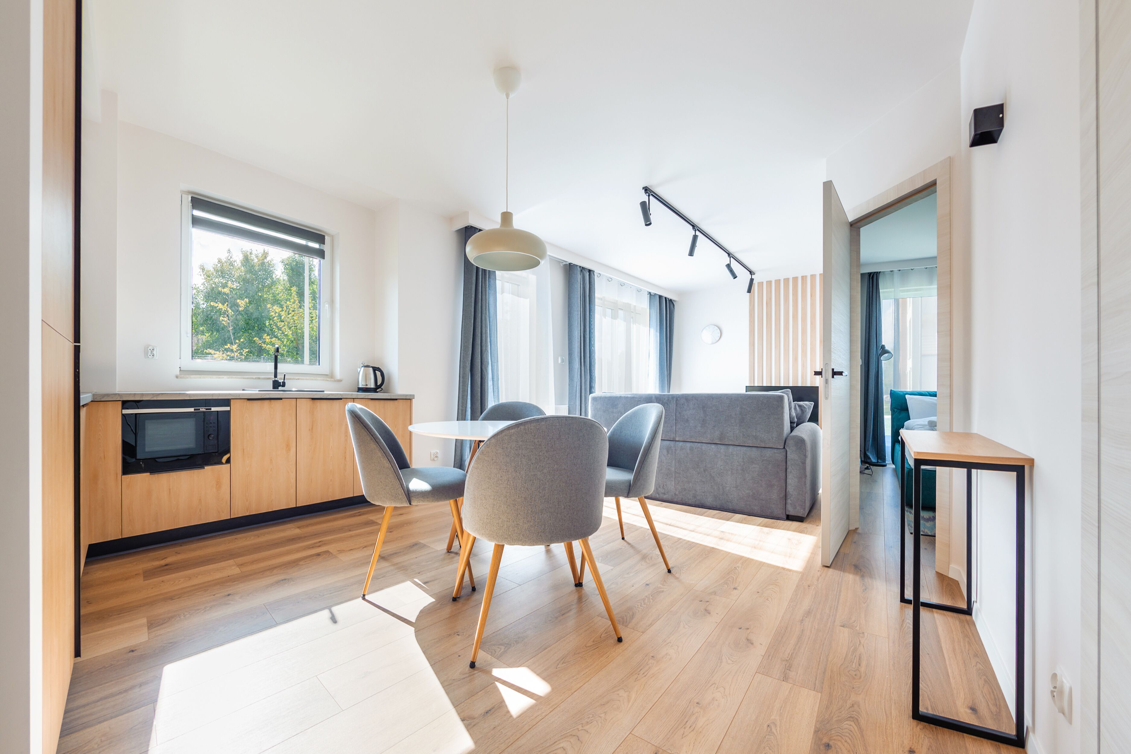 A modern kitchen with wooden cabinets, a built-in microwave, and a dining area with a table and chairs.