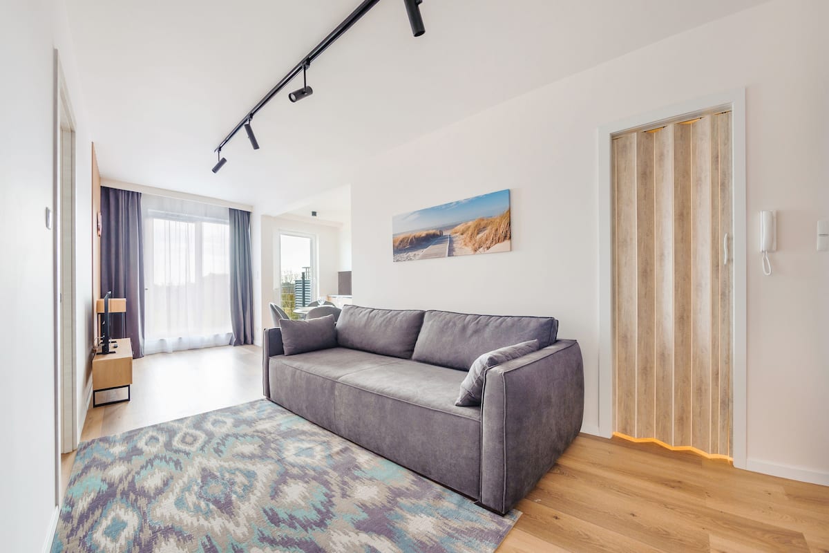 A modern living room with a grey sofa, a patterned rug, and a wooden floor.