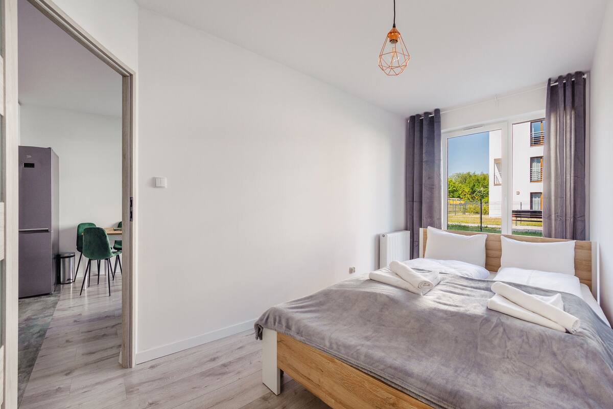 A bedroom with a bed, a desk, and a chair. There is a window with curtains.