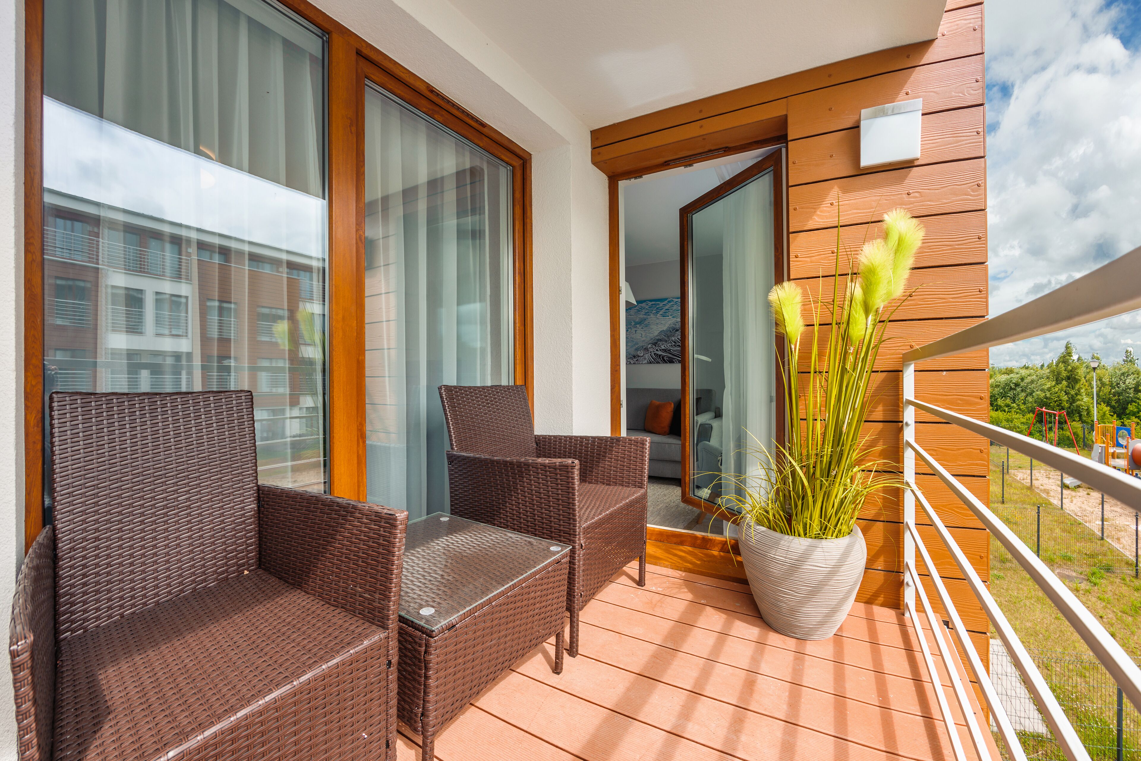 A balcony with wicker furniture, a potted plant, and a view of a building.