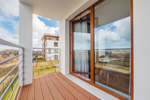 Un balcon doté d’un plancher en bois, d’une porte vitrée et offrant une vue sur un immeuble et un espace verdoyant.