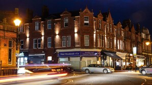 A row of brick buildings with illuminated signs for businesses like Peter Woodcock + Co and Jewellers and Diamond Merchants. - Mode Hotel Lytham (Lytham St. Anne's)
