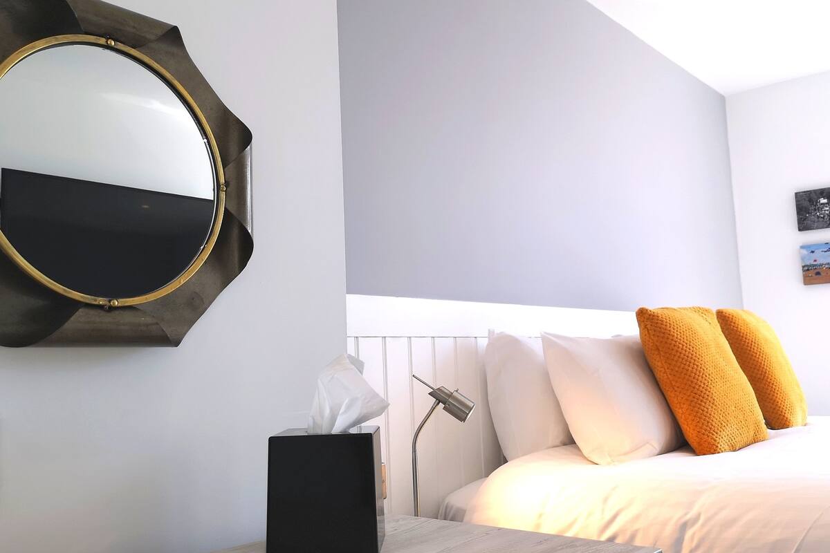A hotel room with a bed, a bedside table with a tissue box, a lamp, and a large mirror on the wall.