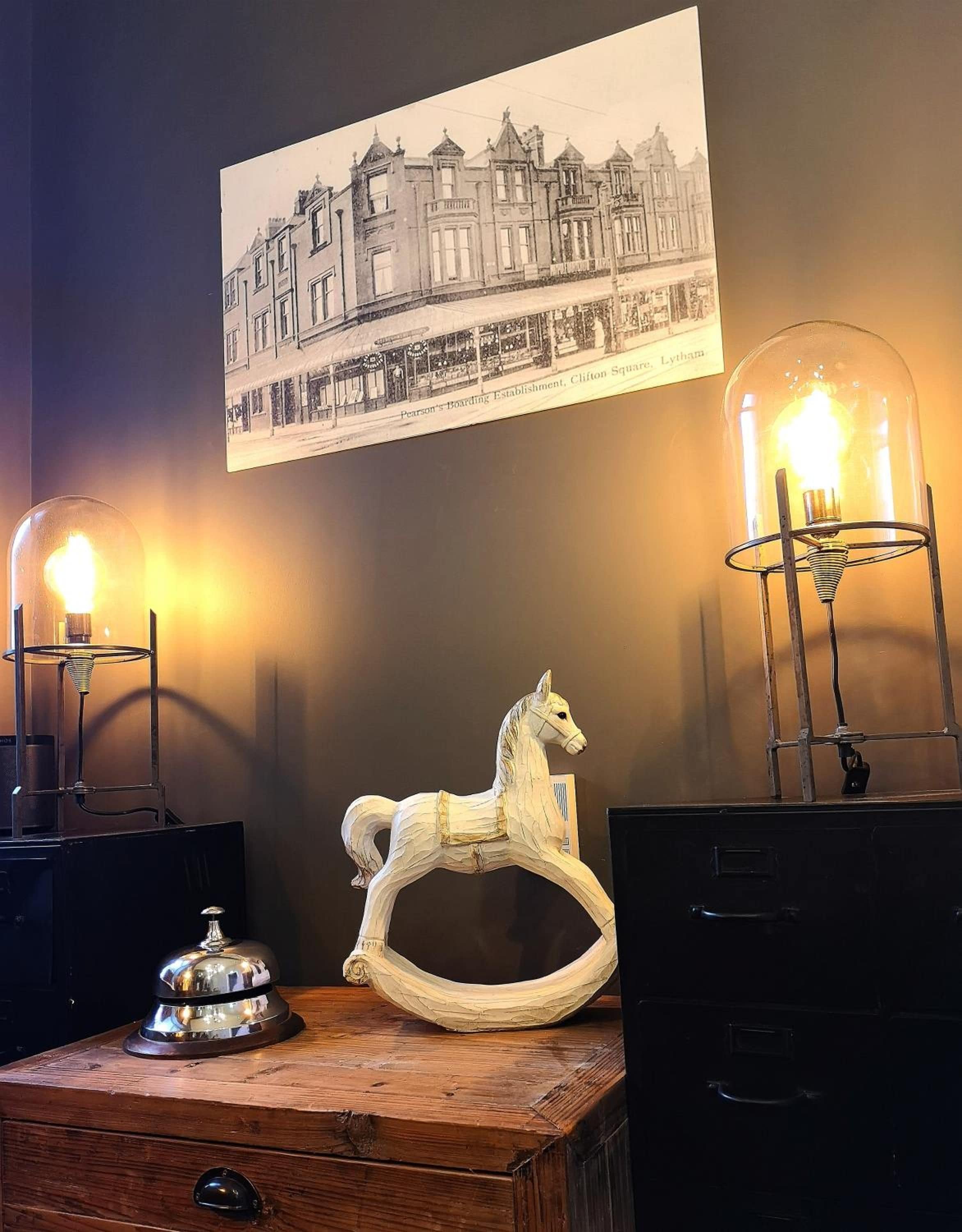 A vintage wooden chest with a horse-shaped ornament, two table lamps with clear glass shades, and a black filing cabinet.